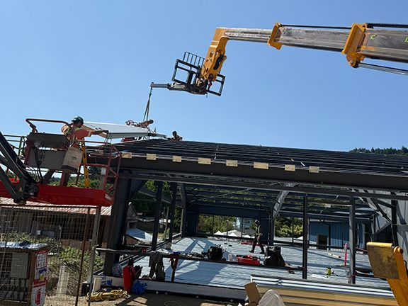 Skilled tradespeople installing metal roofing beams to commercial building project.