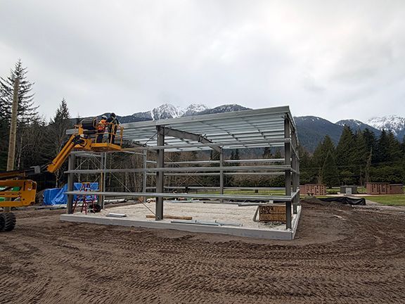 A construction site with a steel building frame with BC mountains in the background.