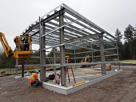 Construction workers assemble the steel frame of a building on a concrete foundation.