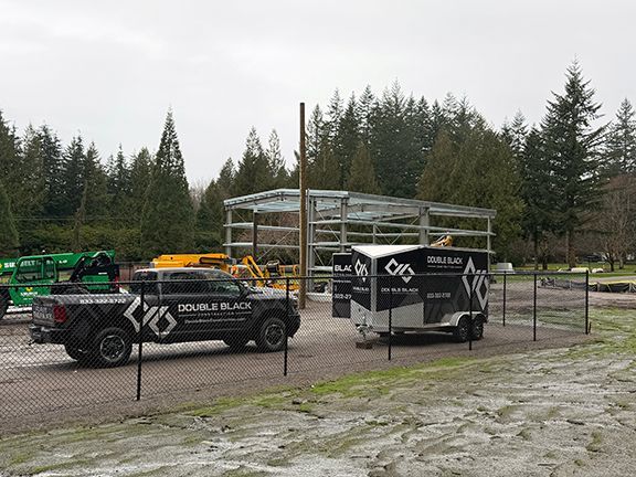 Double Black Construction truck and trailer in front of metal building project in Squamish.