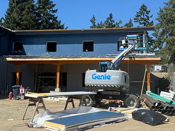 View of elevator crane adding metal roofing panels to building project at Ganges, BC.