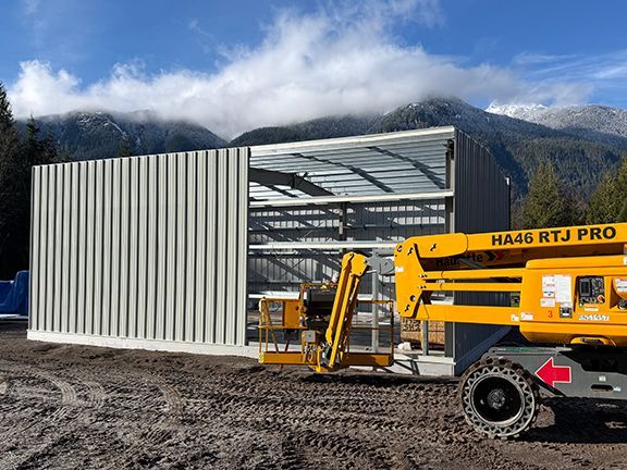 Metal wall panels being added to a pre-engineered steel building against a mountain backdrop.