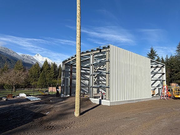 A partially constructed metal-frame maintenance building against the backdrop of mountains of British Columbia.