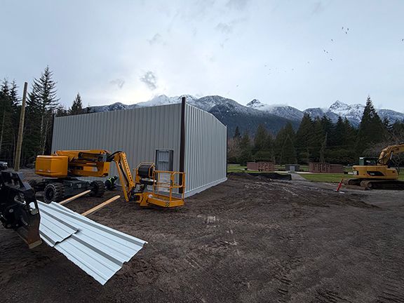 Metal building construction project sits on mountainous site as wall panels get added.