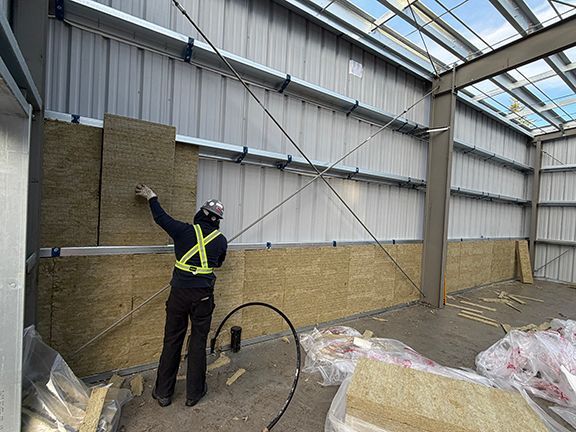 Construction team adds insulation to the walls inside a metal building project.