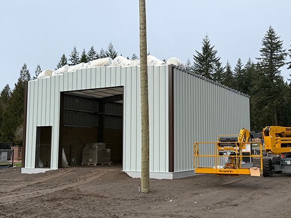 A white metal-sided workshop under construction with roofing materials sitting atop the structure.