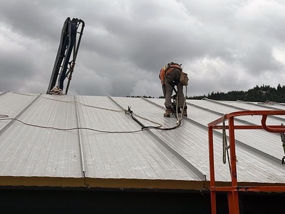 Construction work secures metal panel to roofing system.