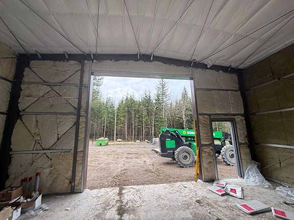 Interior view of a metal building under construction in Squamish, showing insulated walls and a large open doorway.