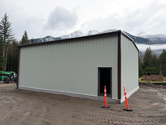 A light-colored metal storage building with a single door on a Squamish jobsite installed by Double Black Construction.