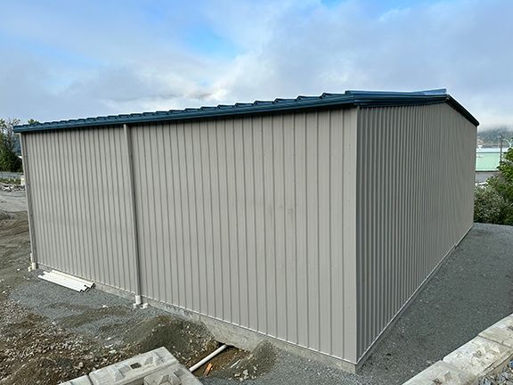 A gray metal building with a black roof is sitting on top of a dirt hill.