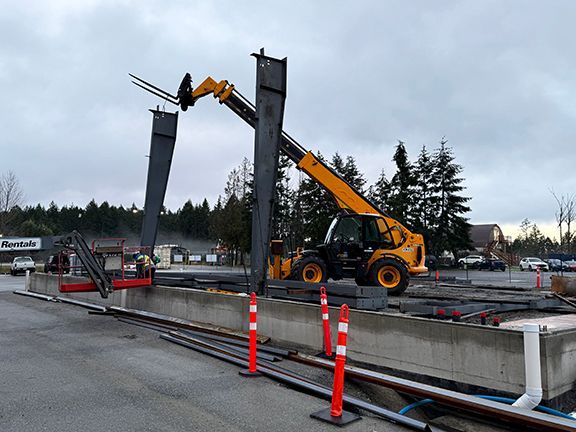 Forklift places steel framing into place on concrete foundation.