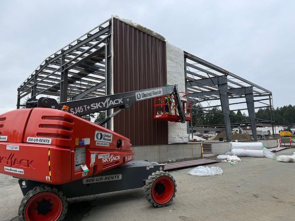 Truck crane adding a steel panel to a pre-engineered metal building in BC.