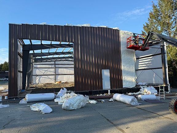 Insulation and brown metal panels being added to steel building frame at BC construction site.