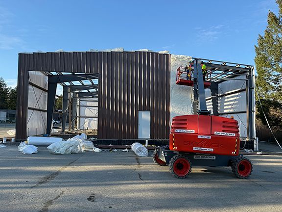 Small lift crane carries skilled tradespeople as they add insulation to pre-engineered steel building in Nanaimo, BC.