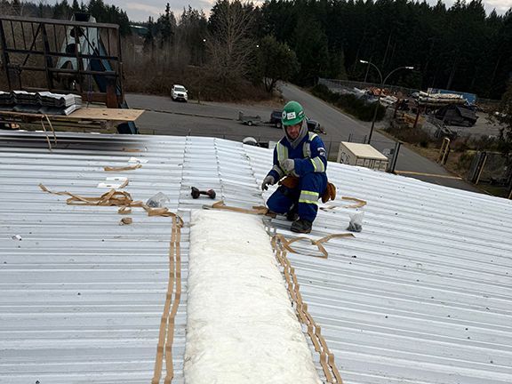 Skilled tradesperson adding ridge cap to the top of a metal building at a project site in British Columbia.