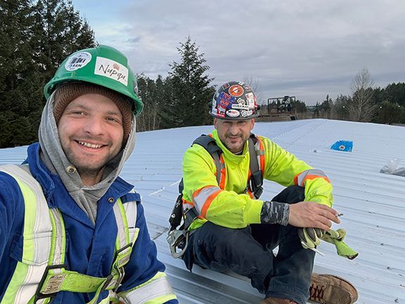 John Lohan sits atop metal building under construction with a member of his team.