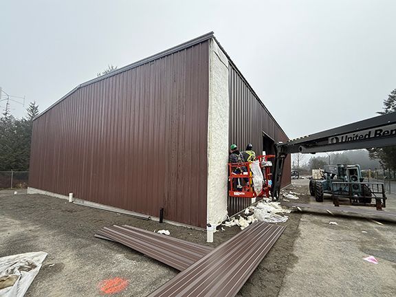 Side view of metal building project in Nanaimo, BC where construction crew is adding final panels to finish job.