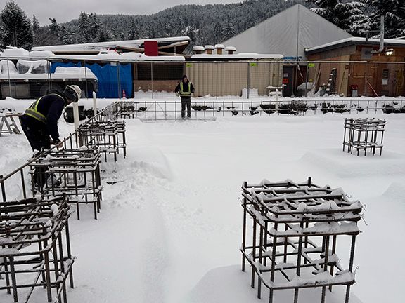 Construction team removes snow from rebar forms on construction site in Salt Spring Island.