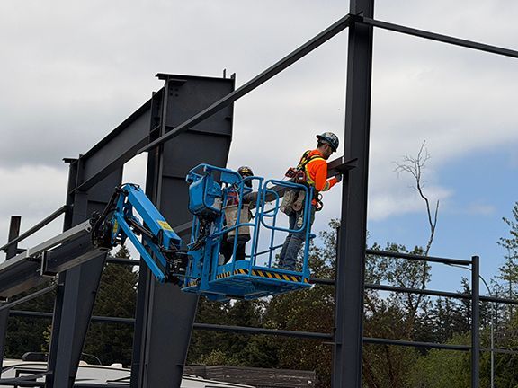 Skilled tradesman lifts and welds steel crossbeam into place at PEMB job.