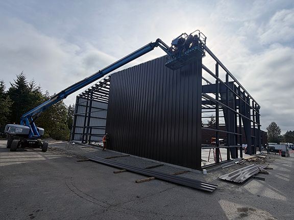 Crew use lift to add metal wall panels to industrial building