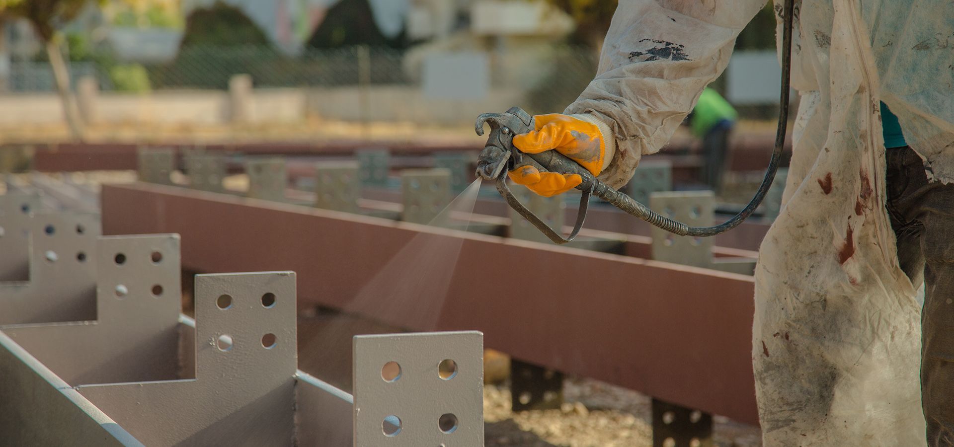 A skilled tradesperson sprays steel framing beams to prevent rust.