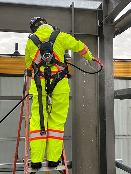 Skilled tradesperson sprays protective coating on steel girder at our YVR building project.