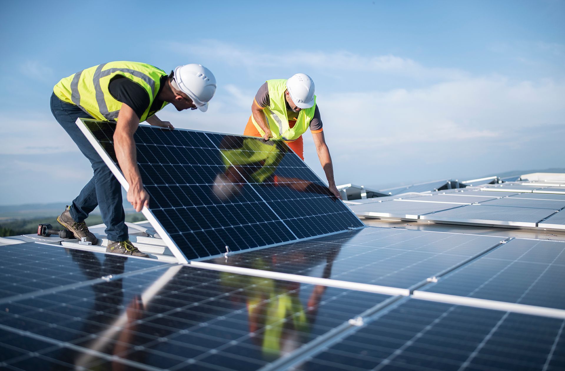 Two skilled tradespeople install a solar panel atop a metal building.