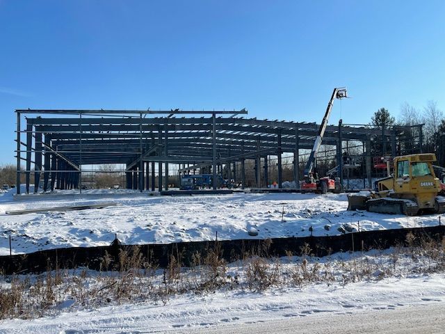 A large building is being built in the snow with a bulldozer in the foreground.