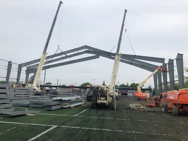 A large metal structure is being built in a parking lot.