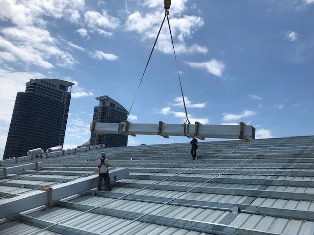 A crane is lifting a pipe on top of a building.