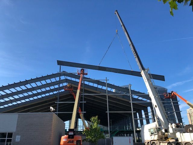 A crane is lifting a metal beam on top of a building under construction.