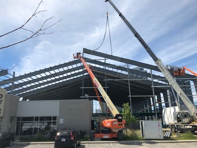 A crane is lifting a metal structure in front of a building under construction.