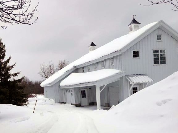 A large white barn is covered in snow