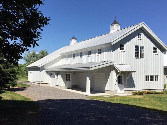 A large white barn with a metal roof is sitting in the middle of a grassy field.