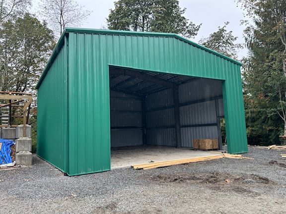 A green metal building with a large door is sitting on top of a gravel road.