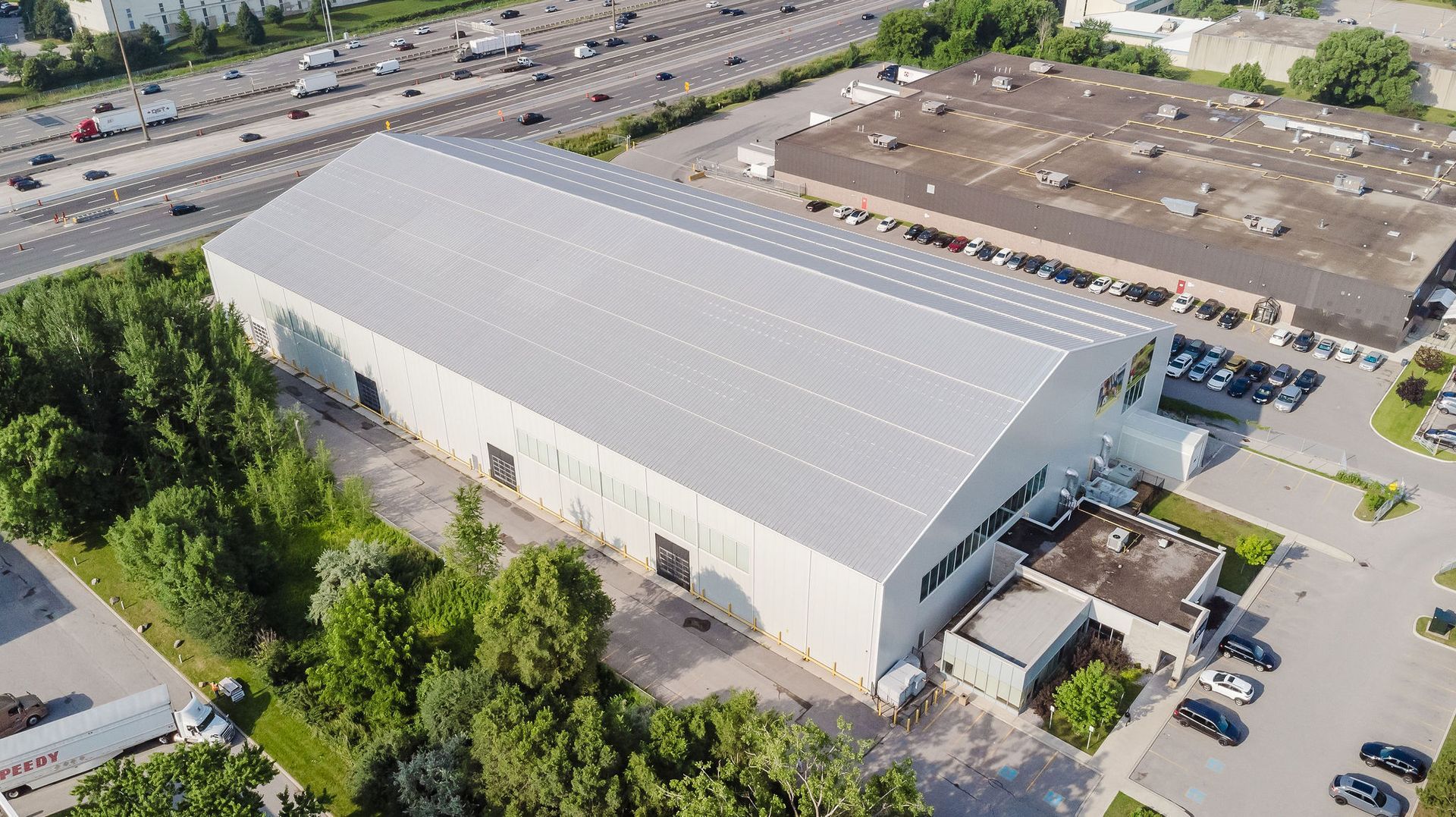 An aerial view of a large warehouse surrounded by trees and a highway.