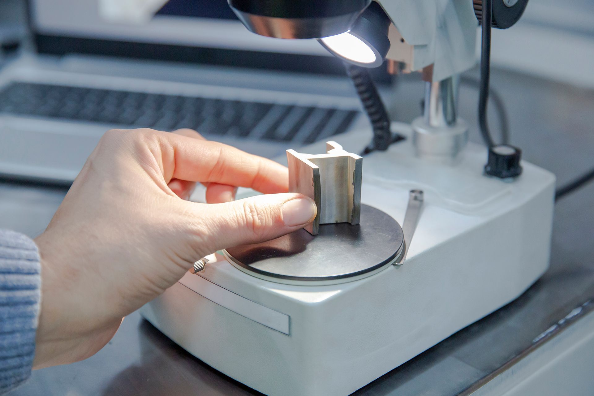 A person is holding a piece of metal under a microscope.