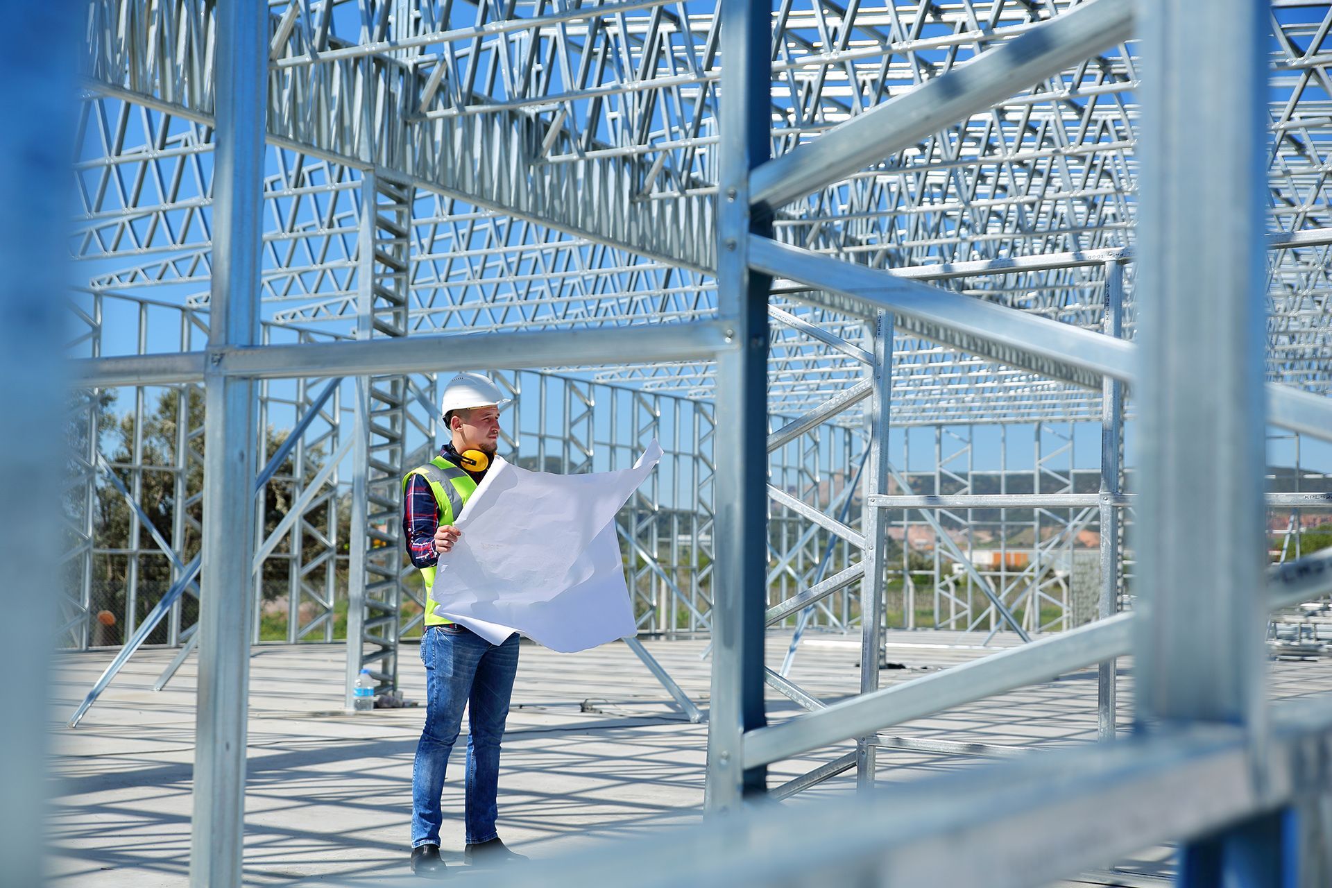 A man is standing in front of a building under construction holding a blueprint.