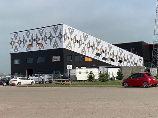 A red car is parked in front of a large building.