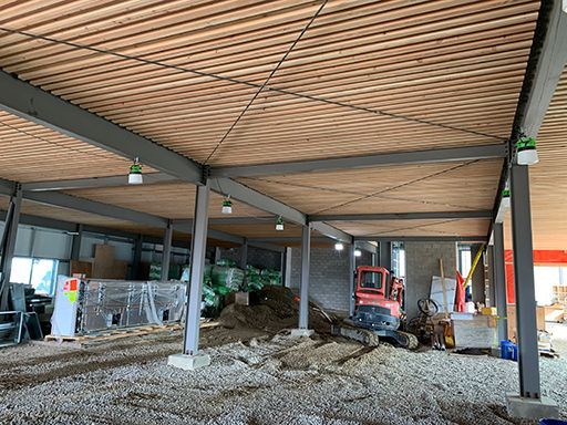 A building under construction with a wooden ceiling and a tractor in the background.