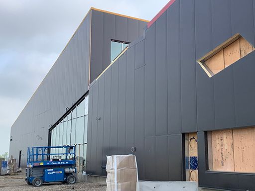 A blue scissor lift is parked in front of a large building under construction.