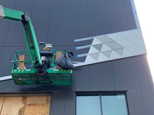 A construction worker is installing a tile on the side of a building.