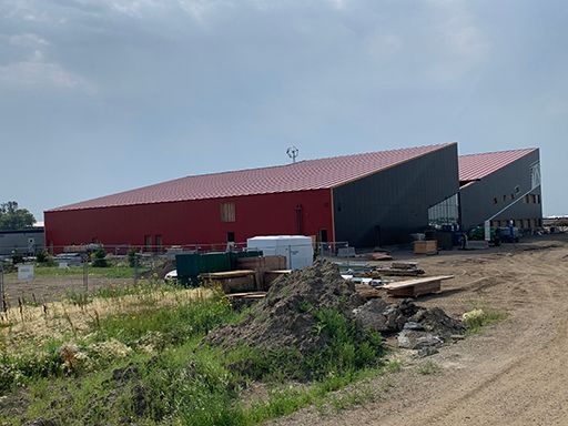 A large red building is being built next to a dirt road.