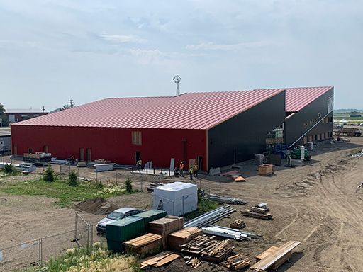 A large building with a red roof is being built in a dirt field.