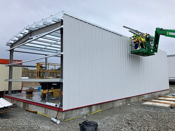 A green crane is lifting a piece of metal on top of a building under construction.