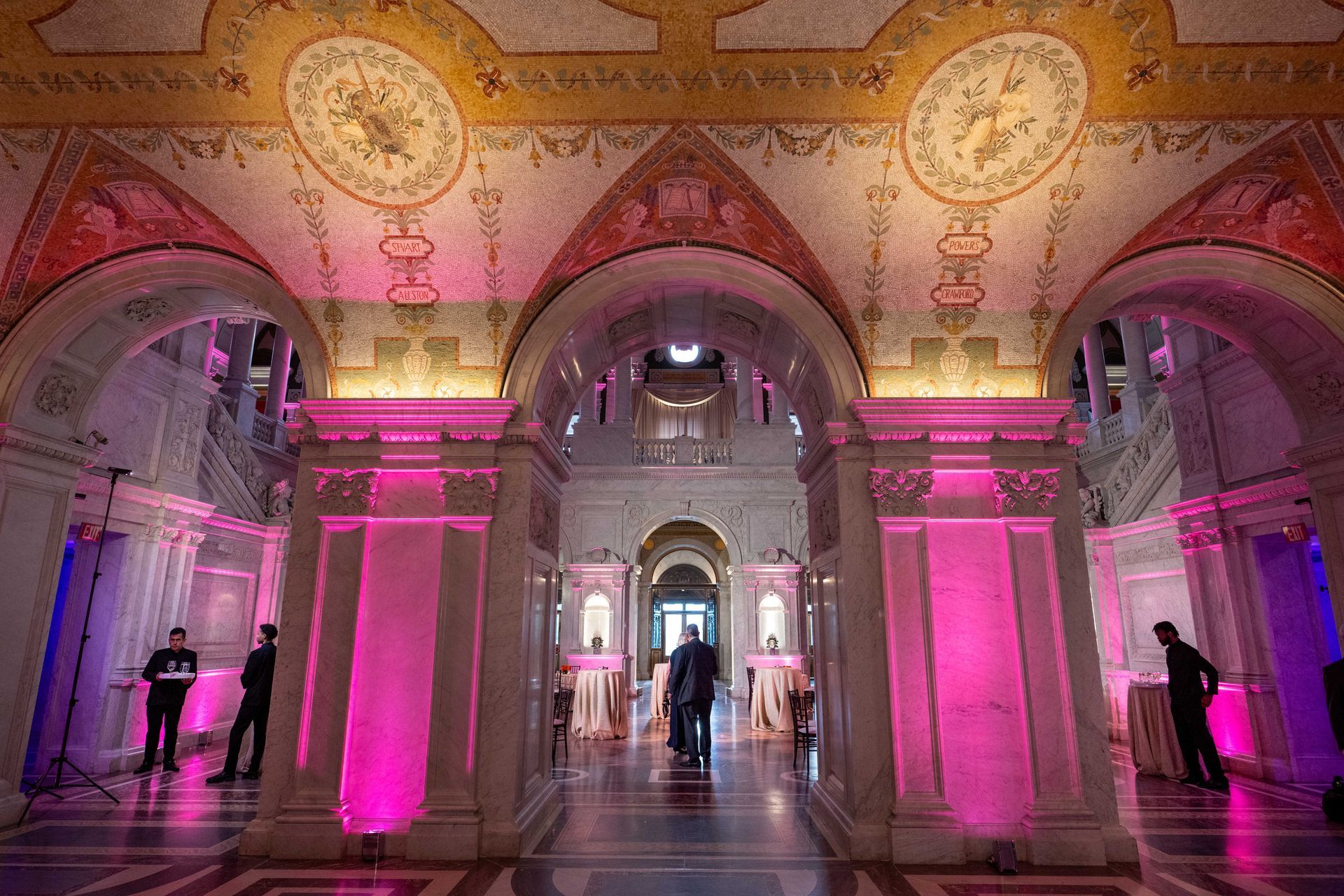 A large hallway in a building with pink lights on the walls and columns.