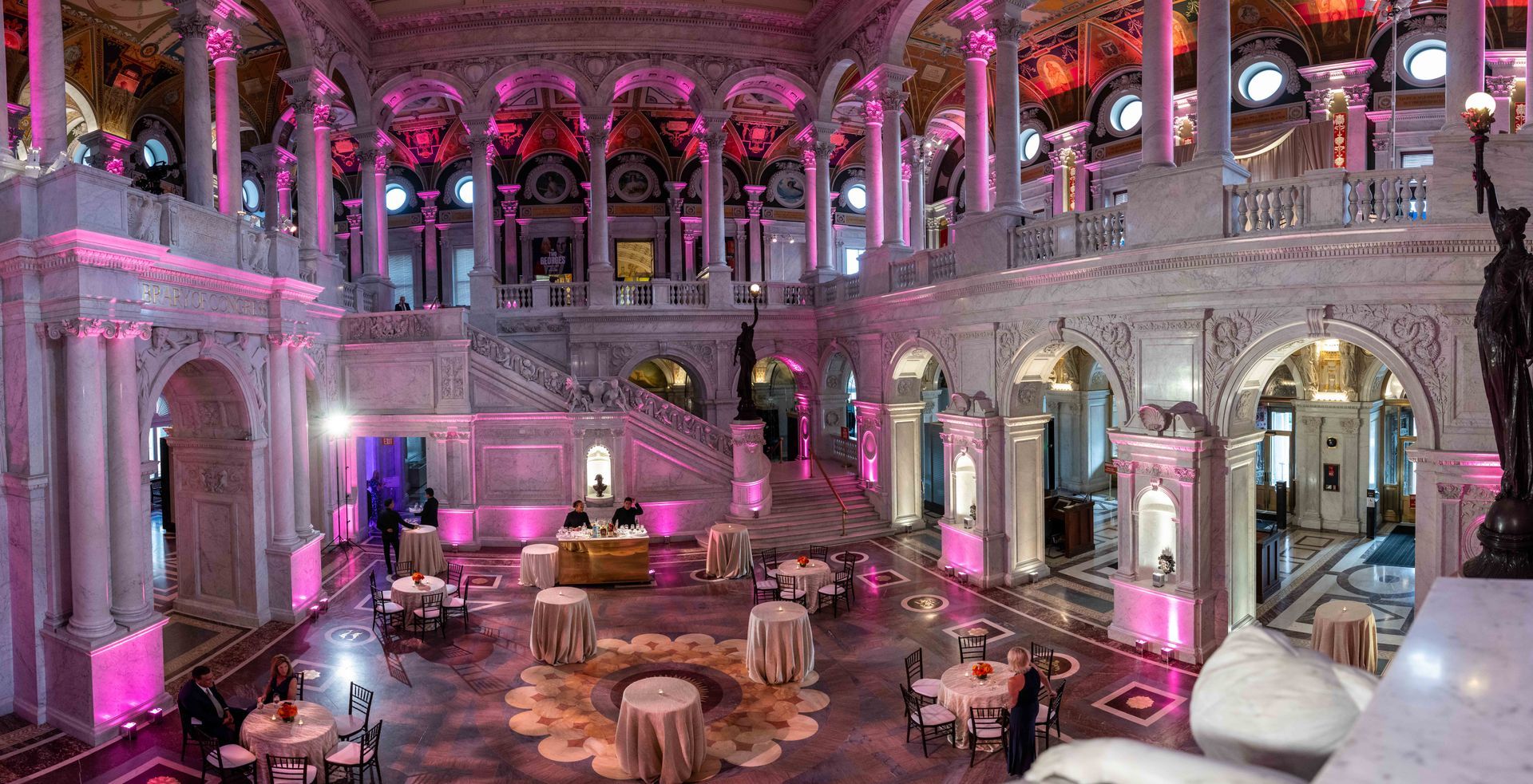 A large room with tables and chairs in it is decorated with pink lights.