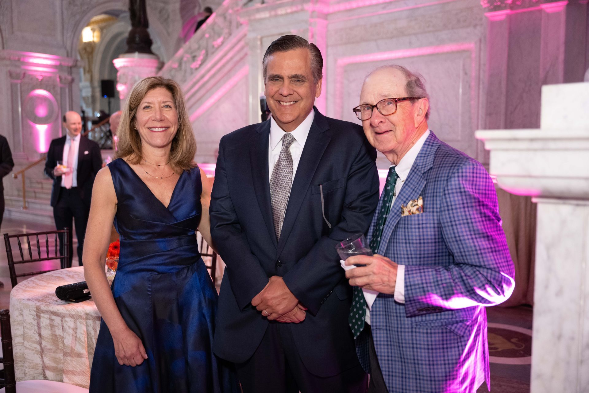 A woman in a blue dress is standing next to two men in suits.
