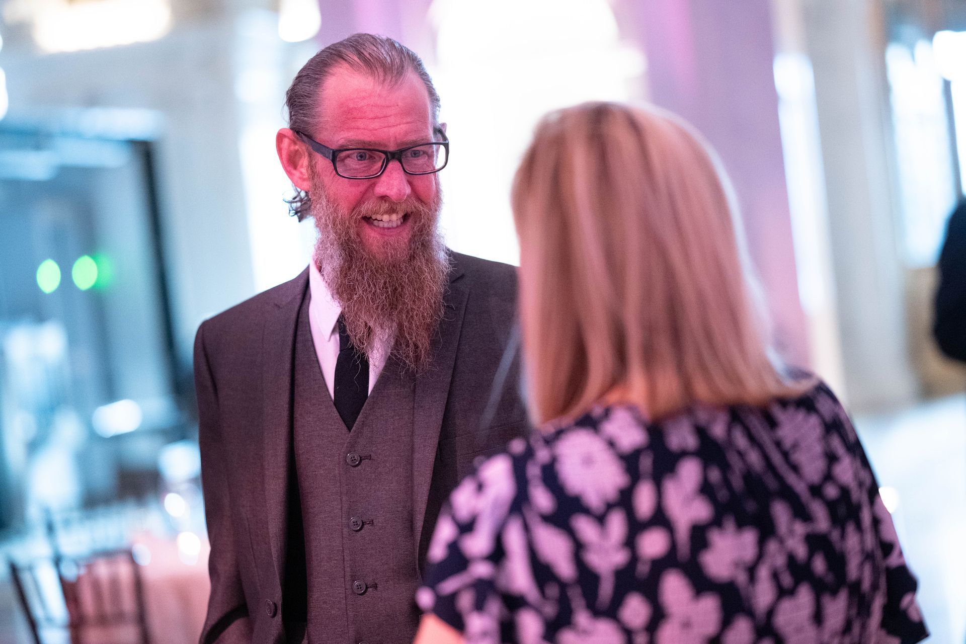 A man with a beard and glasses is talking to a woman.