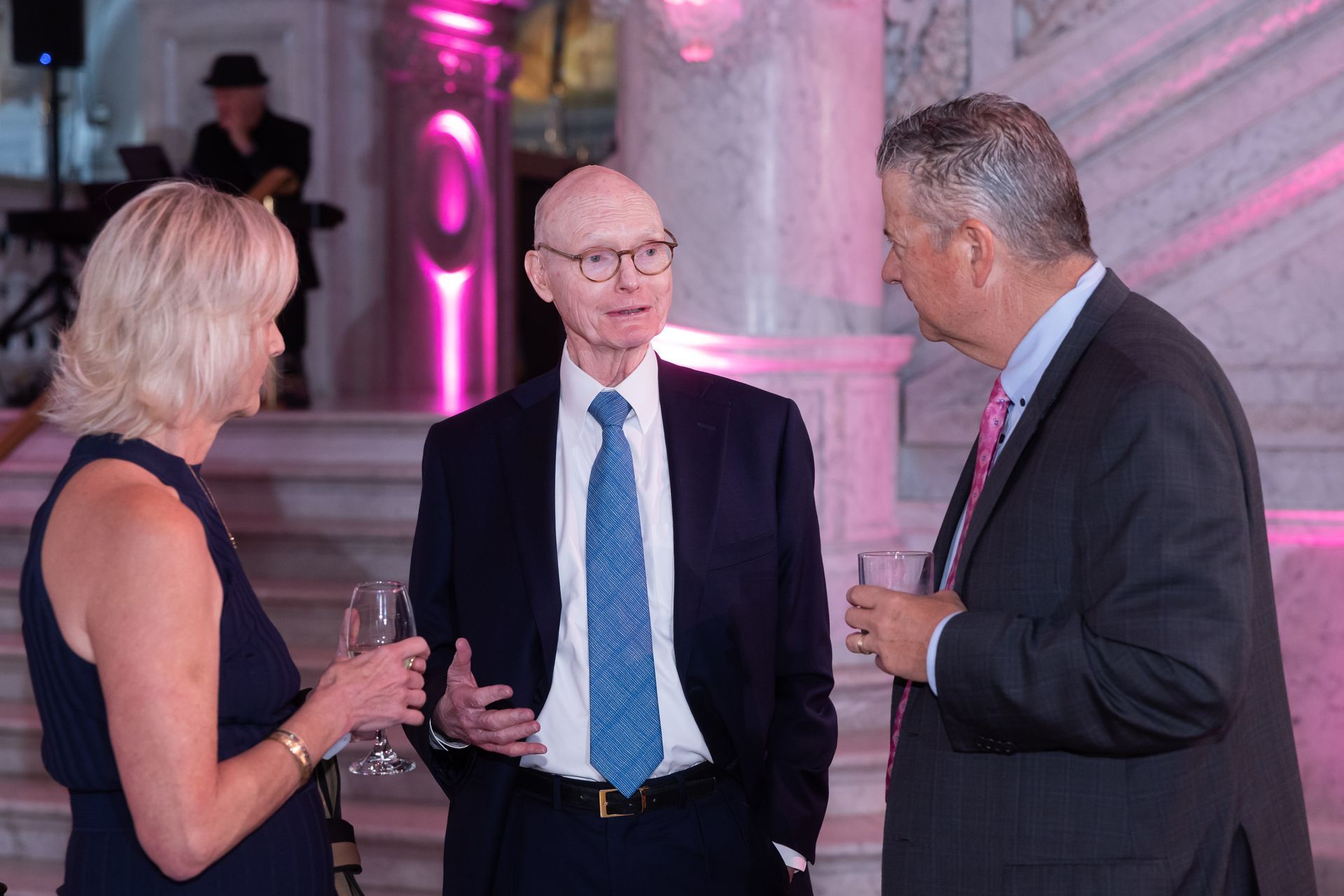 A man in a suit and tie is talking to two other men and a woman.